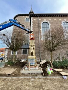 het oorlogsmonument in Zonhoven wordt met een blauwe kraan terug geplaatst met op de achtergrond de kerk.