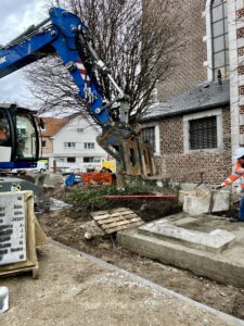 De blauwe kraan is ze onderste stenen aan het opheffen om ze terug te plaatsen met de kerk van Zonhoven op de achtergrond.