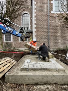 twee mannen , een met veiligheidshelm en vest en een andere werkman zijn de onderste stenen met behulp van een blauwe kraan aan het terugplaatsen.